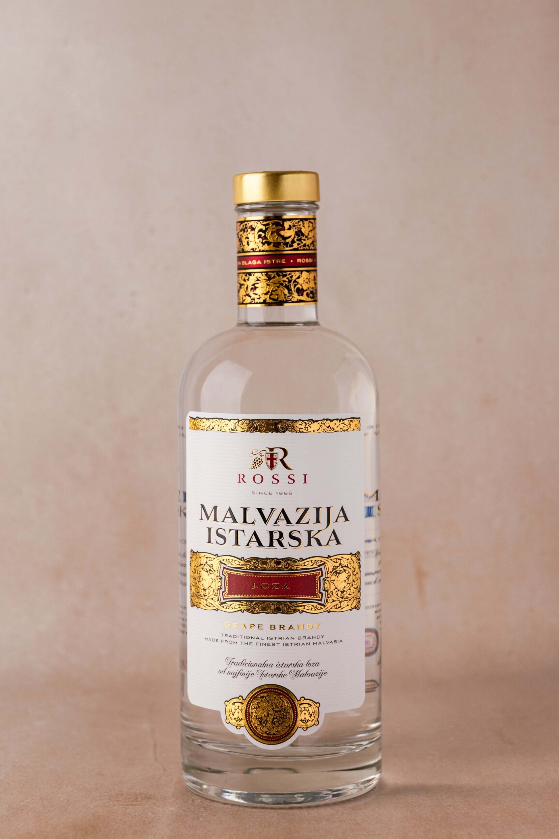 Bottle of Rossi Loza Malvazija Istarska premium brandy with golden label and cap on a neutral background.